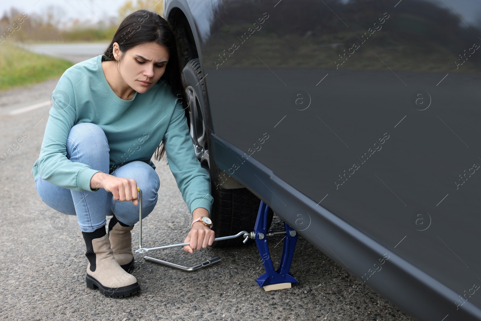 Photo of Young woman changing tire of car on roadside