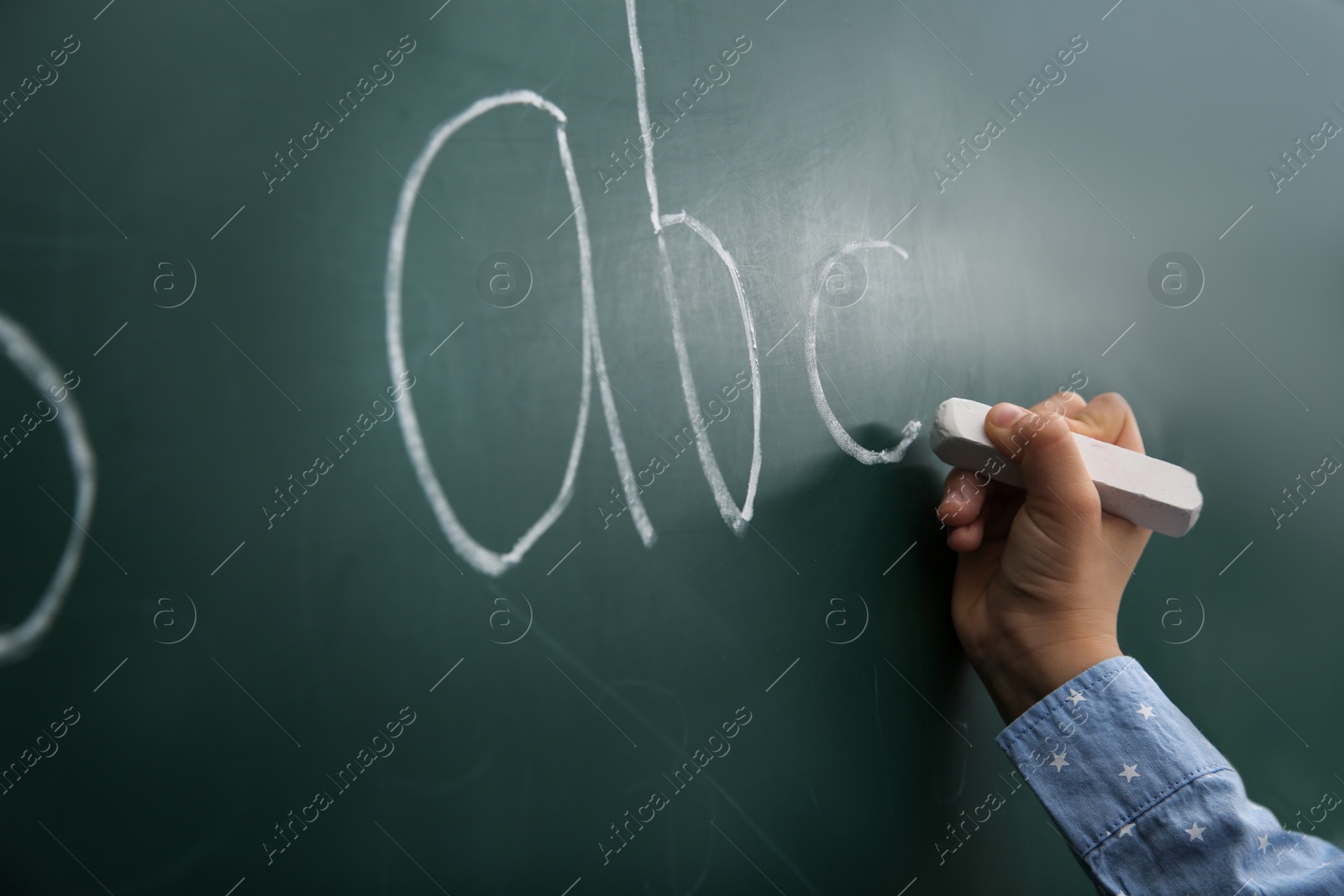 Photo of Little child writing letters on chalkboard, closeup