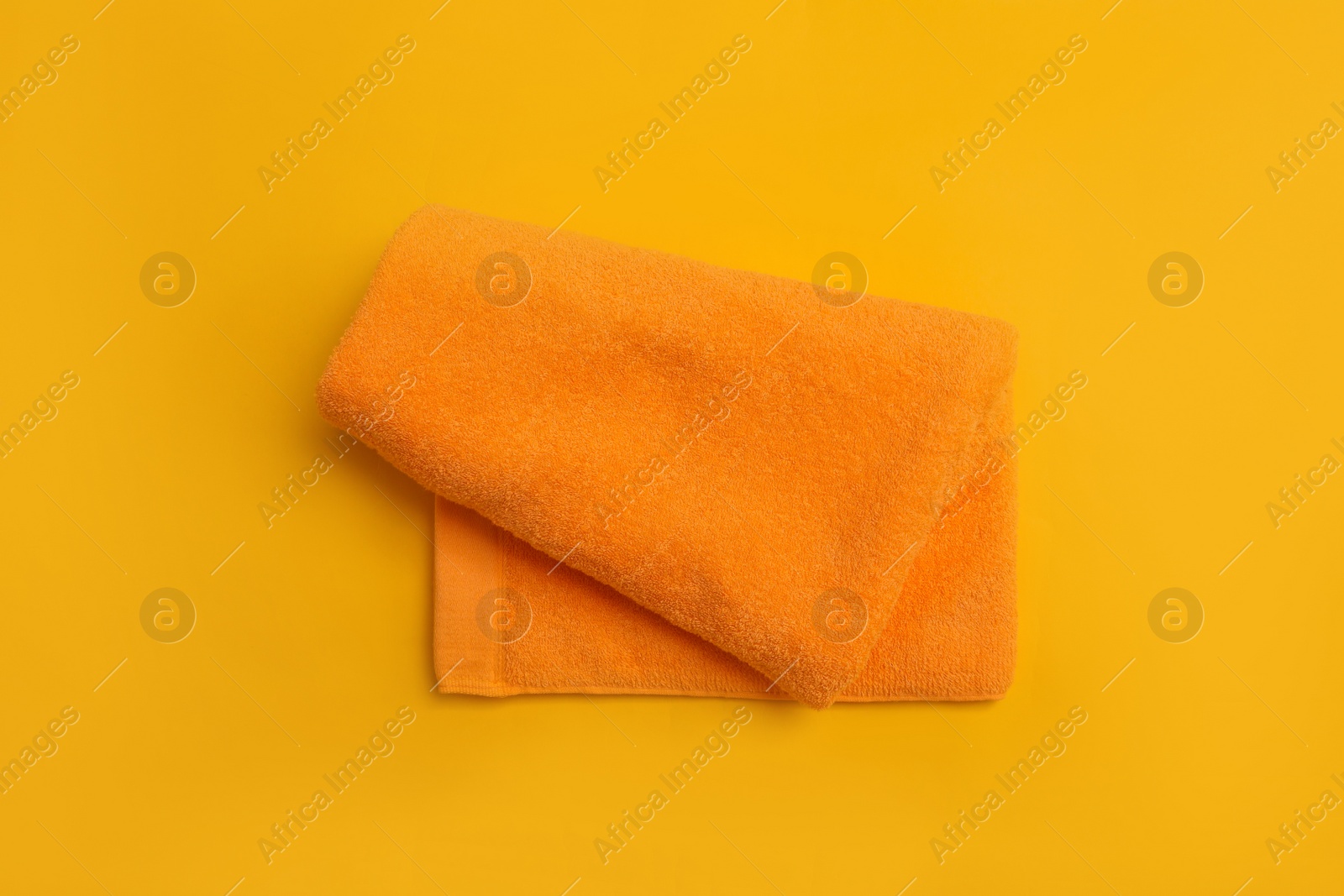 Photo of Folded orange beach towel on yellow background, top view