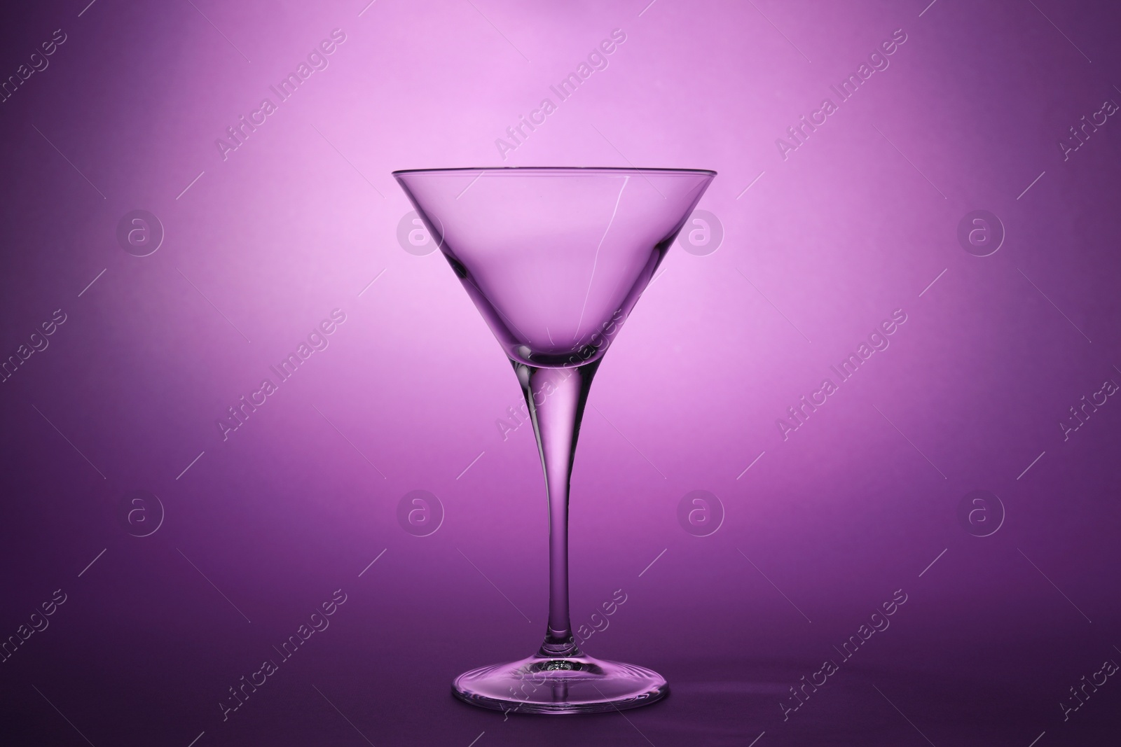 Photo of Elegant empty martini glass on purple background