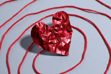 Red crumpled paper heart and thread on gray background, closeup