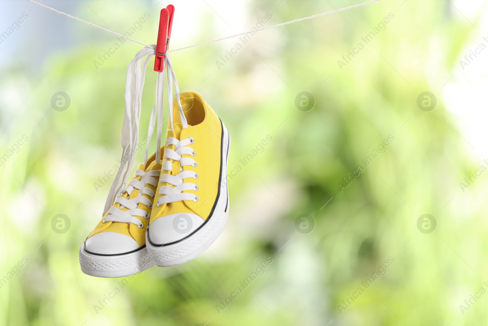 Photo of Stylish sneakers drying on washing line against blurred background, space for text