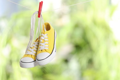 Photo of Stylish sneakers drying on washing line against blurred background, space for text