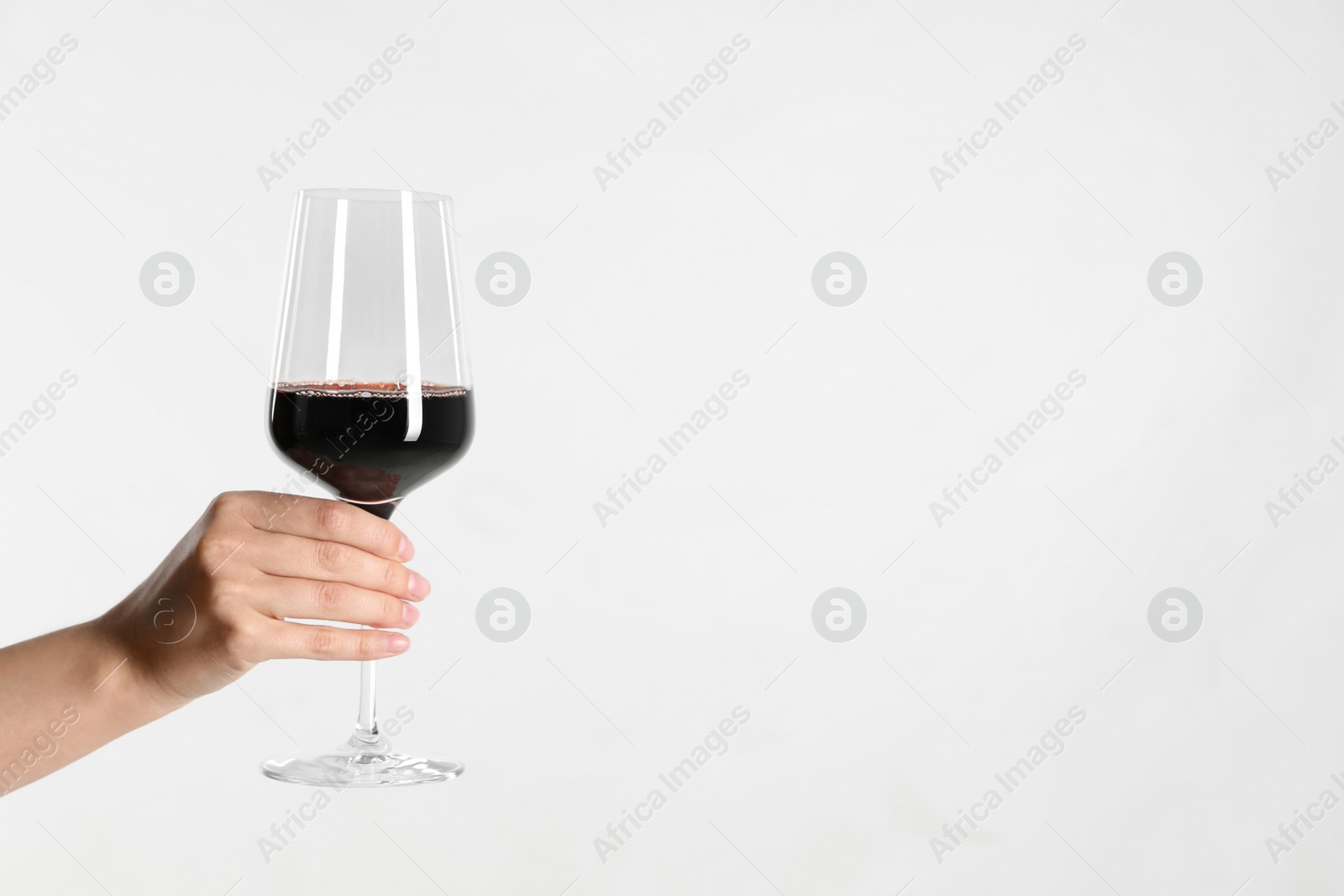 Photo of Woman holding glass of red wine on light background, closeup. Space for text