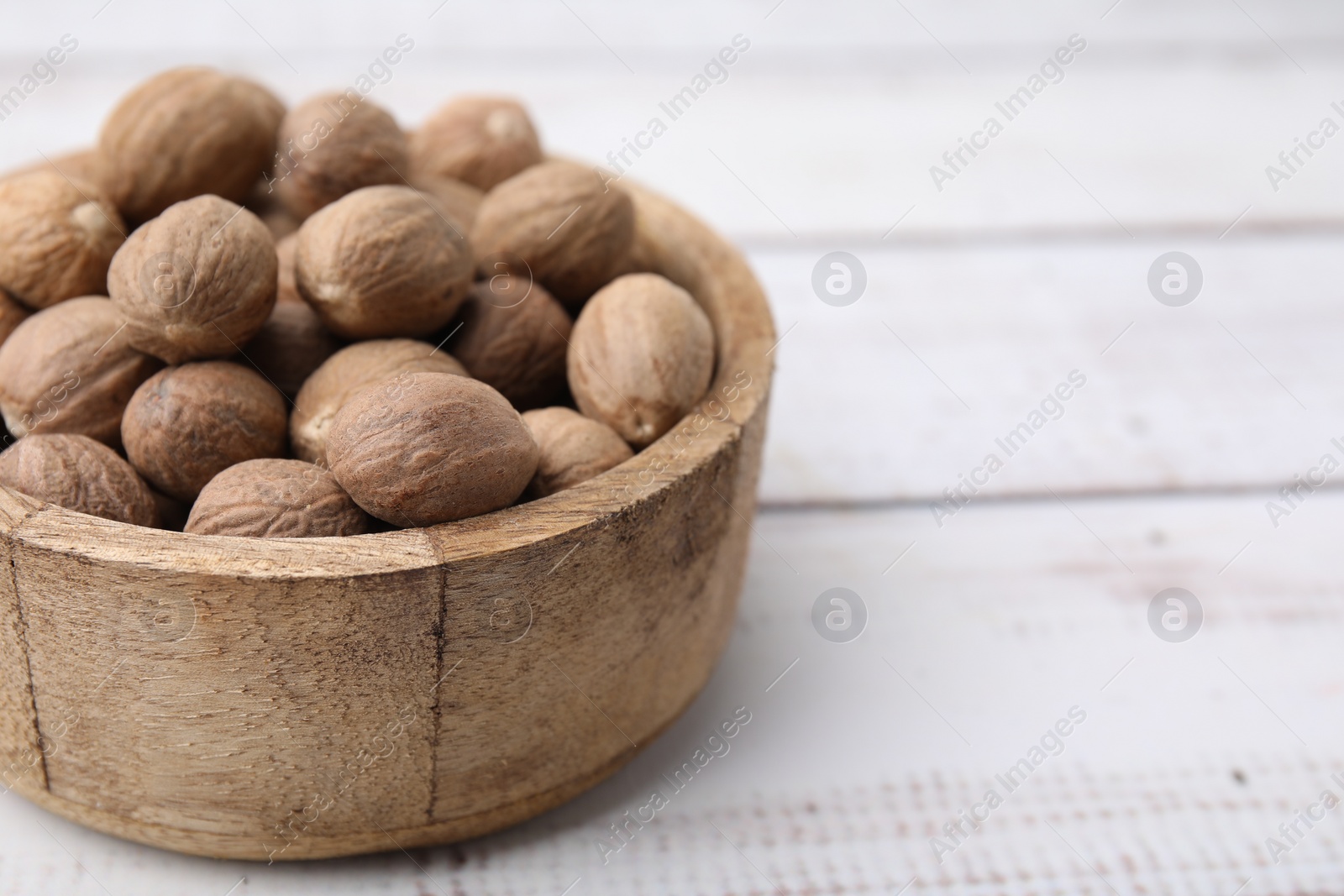 Photo of Whole nutmegs in bowl on light wooden table, closeup. Space for text