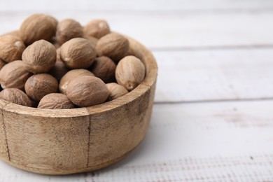 Whole nutmegs in bowl on light wooden table, closeup. Space for text