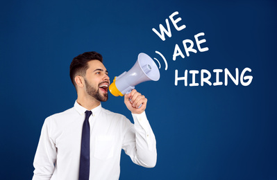 Image of Young man with megaphone and phrase WE ARE HIRING on blue background. Career promotion