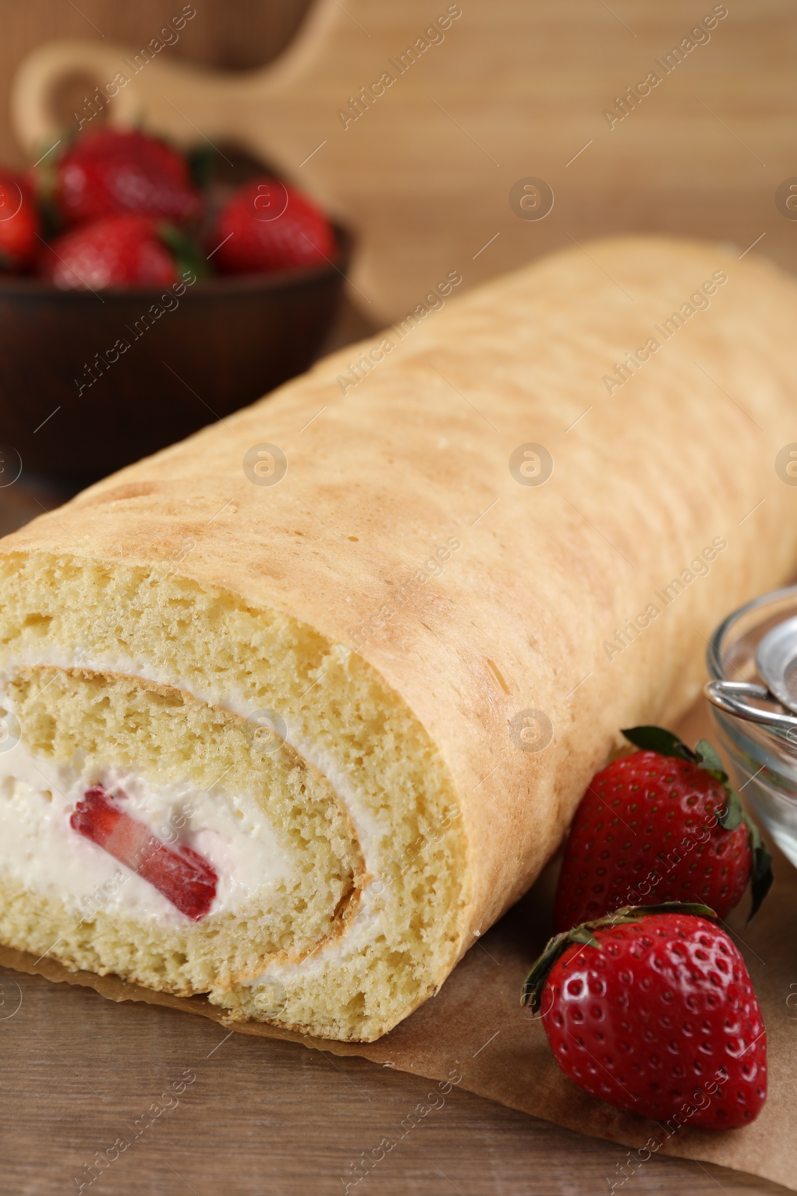 Photo of Delicious sponge cake roll with strawberries and cream on wooden table, closeup