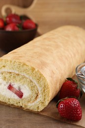 Photo of Delicious sponge cake roll with strawberries and cream on wooden table, closeup