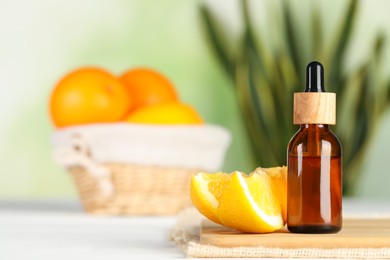 Bottle of essential oil and orange on white wooden table, space for text