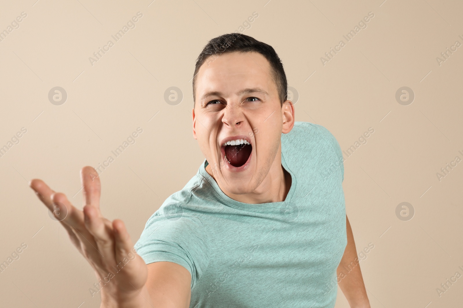 Photo of Handsome young man shouting on beige background