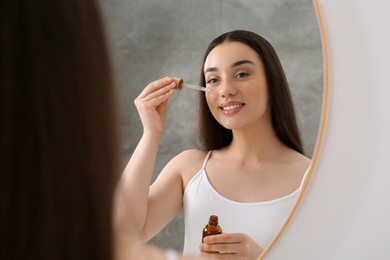 Photo of Woman applying essential oil onto face near mirror