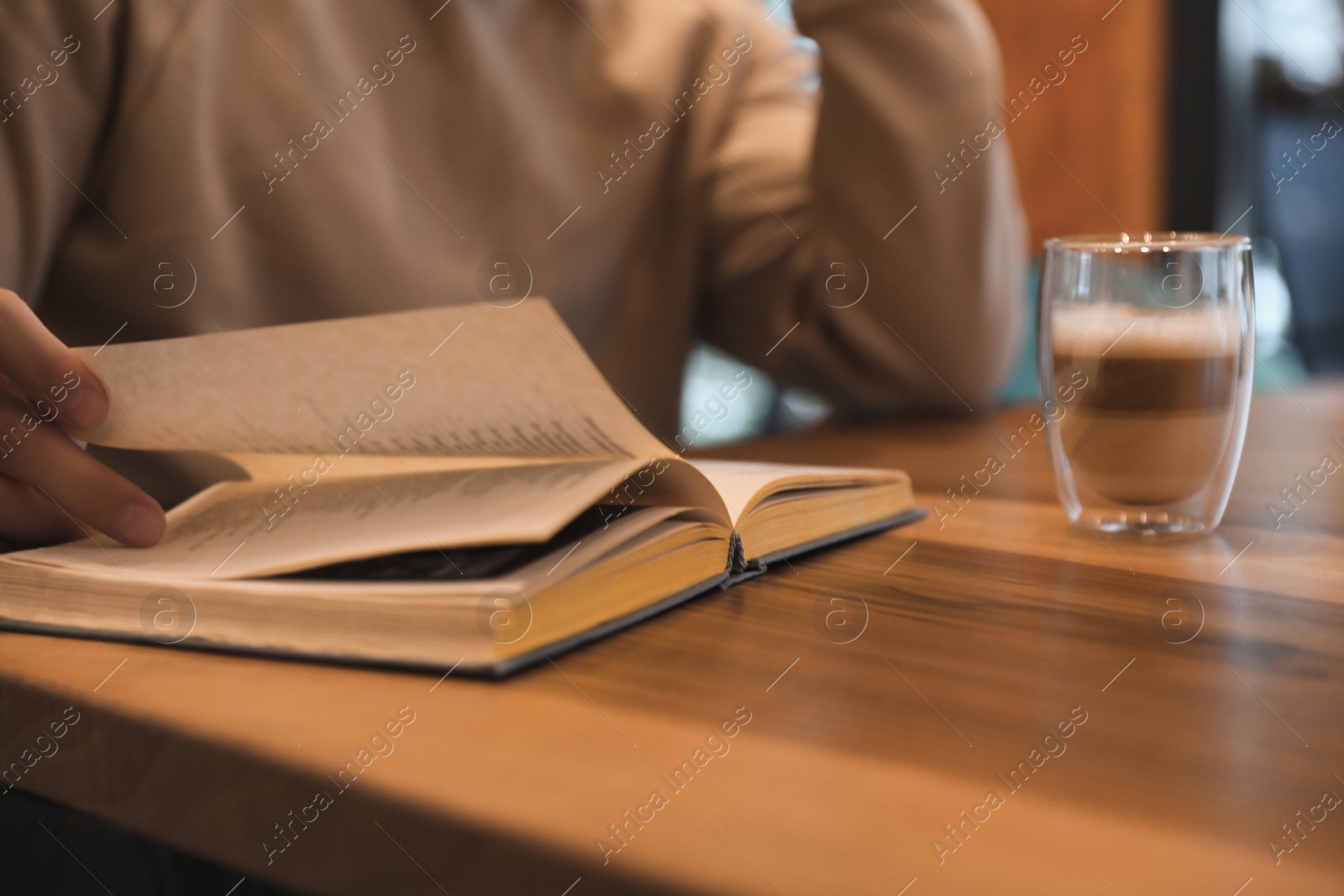 Photo of Man with coffee reading book at wooden table, closeup