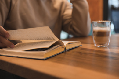 Man with coffee reading book at wooden table, closeup