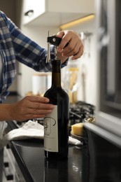 Photo of Woman opening wine bottle with corkscrew at black countertop indoors, closeup