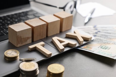 Photo of Word Tax made of wooden letters, cubes, laptop, banknotes and coins on grey table