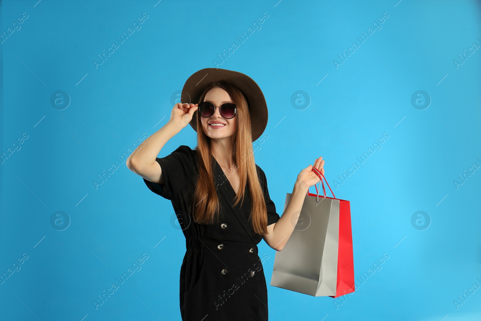 Photo of Beautiful young woman with paper shopping bags on light blue background