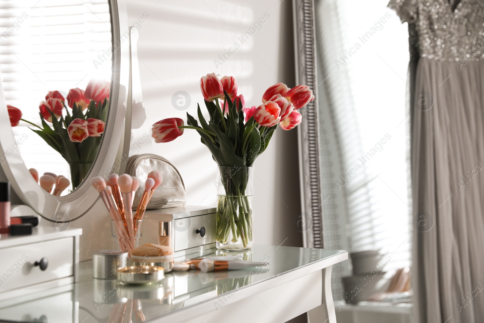 Photo of Elegant dressing table with makeup products, accessories and tulips indoors. Interior element