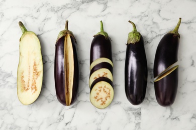 Cut and whole eggplants on white marble table, flat lay