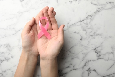 Photo of Woman holding pink ribbon on marble background, top view with space for text. Breast cancer awareness concept