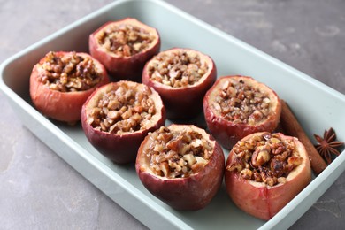 Tasty baked apples with nuts, honey and spices in dish on gray table, closeup