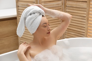 Beautiful woman taking bath with foam in tub indoors