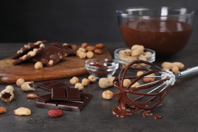 Whisk with chocolate cream and ingredients on gray table, closeup