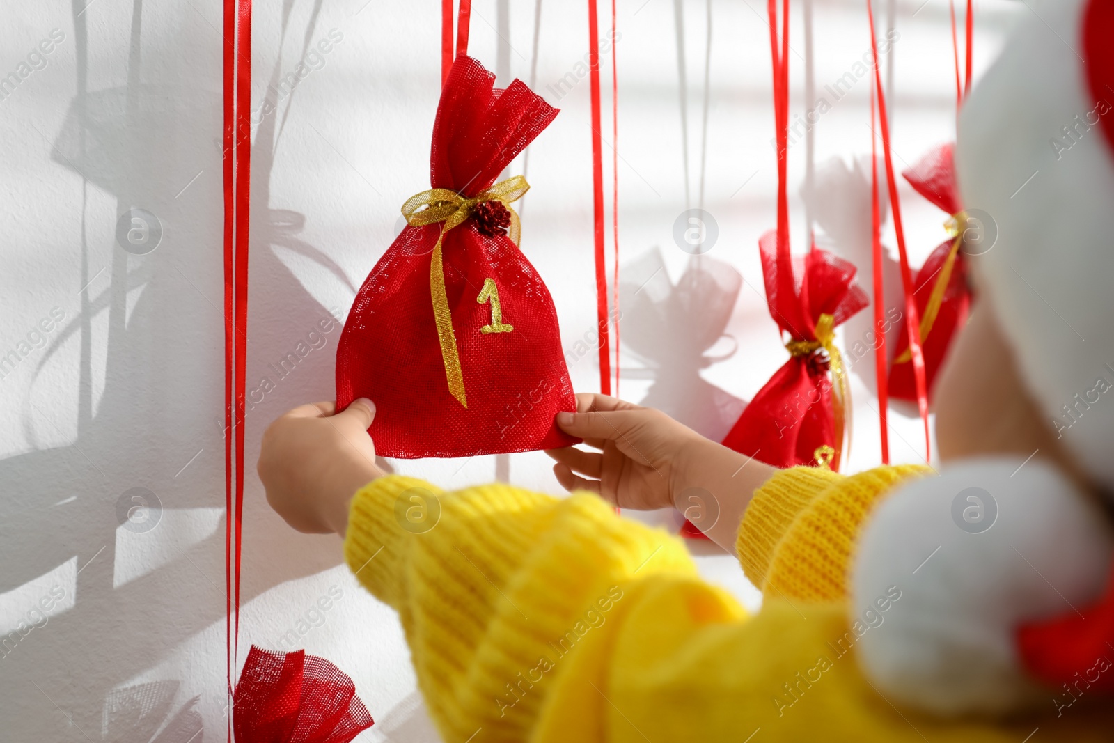 Photo of Little girl taking gift from Christmas advent calendar indoors, closeup