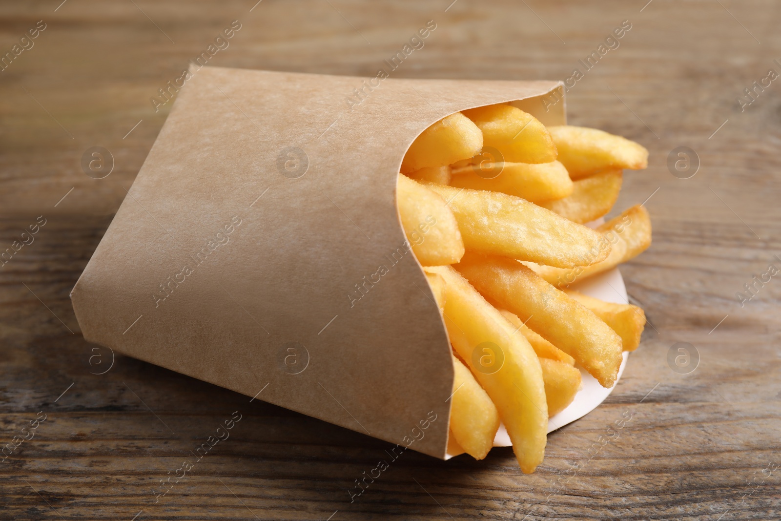 Photo of Delicious French fries in paper cup on wooden table, closeup