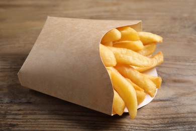 Delicious French fries in paper cup on wooden table, closeup