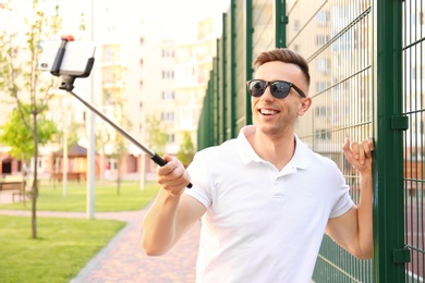 Photo of Young man taking selfie with monopod outdoors