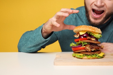 Young man with tasty huge burger at table
