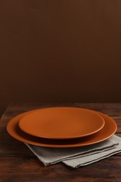 Photo of Beautiful ceramic plates and napkin on wooden table against brown background, space for text