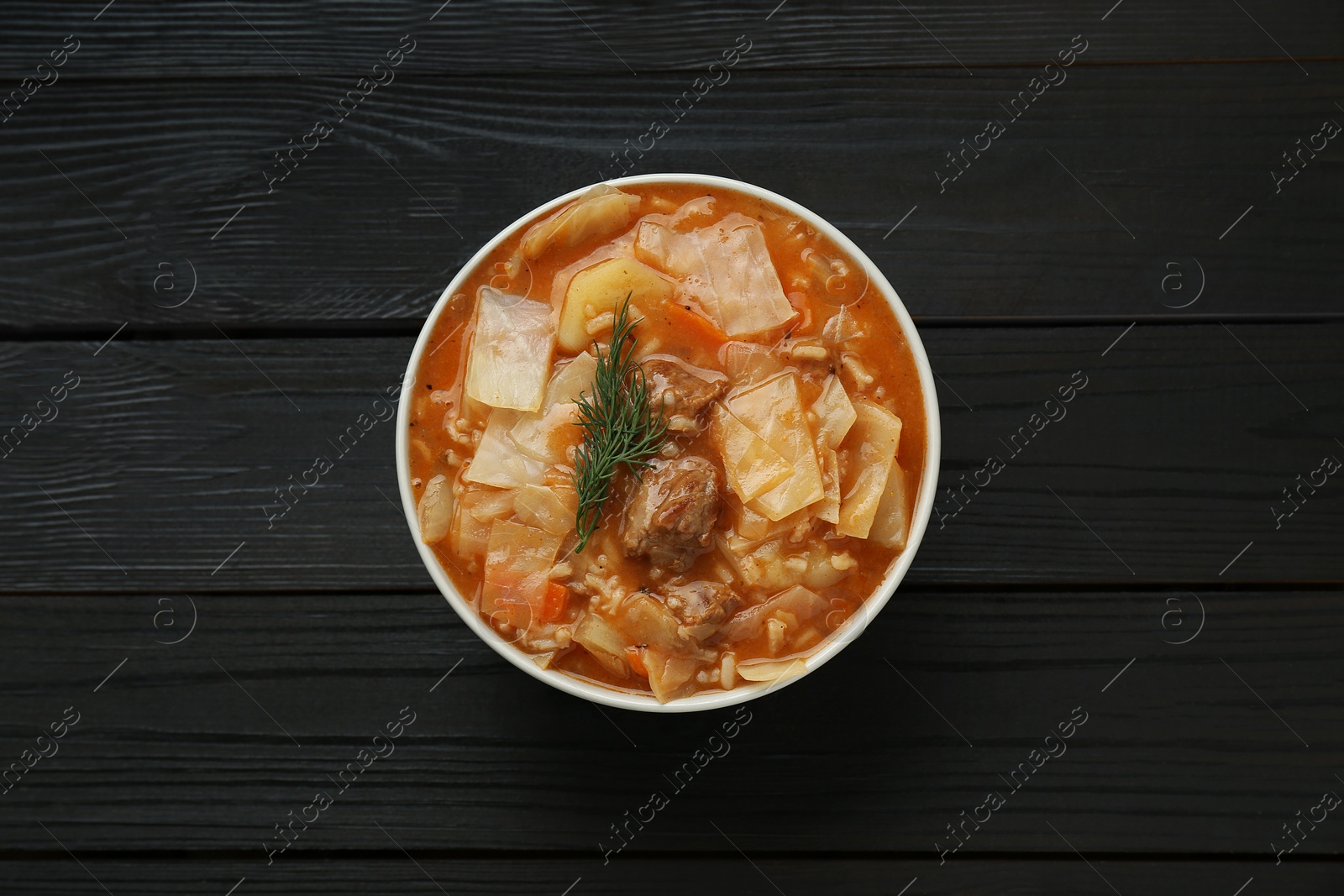Photo of Tasty cabbage soup with meat, carrot and dill on black wooden table, top view