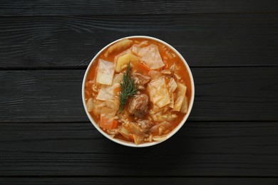 Tasty cabbage soup with meat, carrot and dill on black wooden table, top view