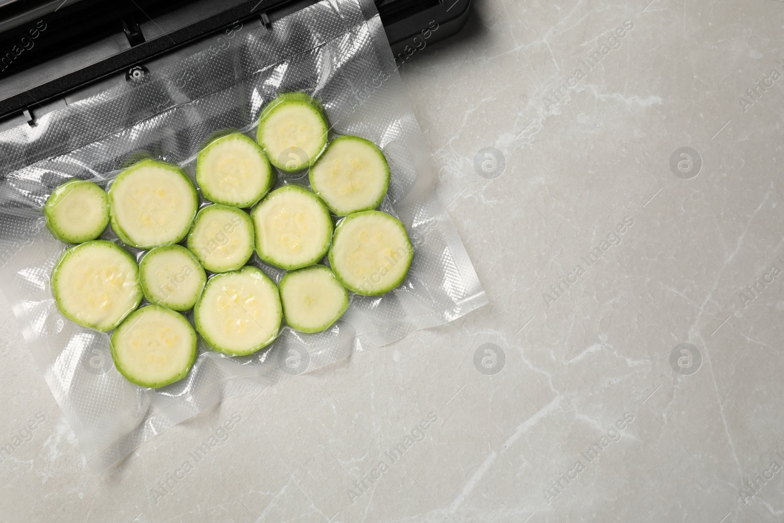 Photo of Sealer for vacuum packing and plastic bag with cut zucchini on light grey marble table, top view. Space for text
