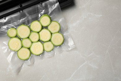 Photo of Sealer for vacuum packing and plastic bag with cut zucchini on light grey marble table, top view. Space for text