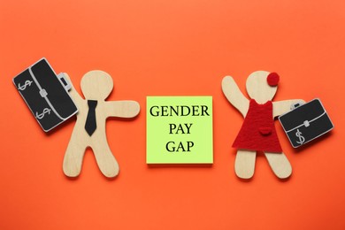 Photo of Gender pay gap. Wooden figures of man and woman, paper note on orange background, flat lay