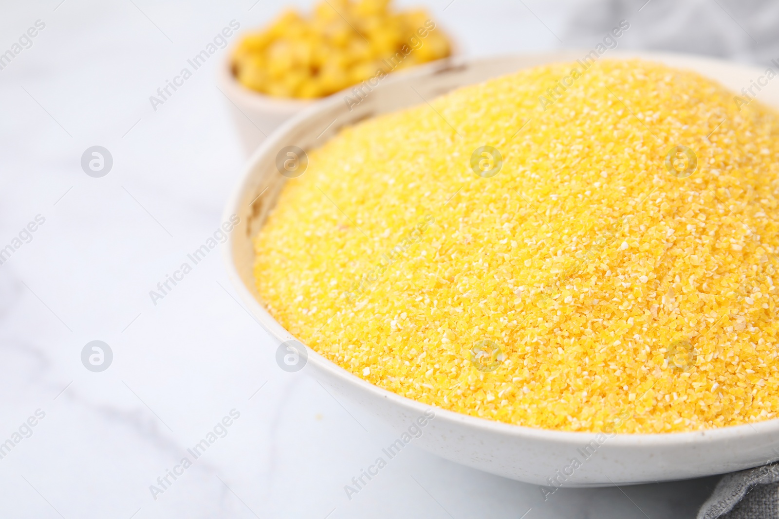 Photo of Raw cornmeal in bowl on white marble table, closeup. Space for text