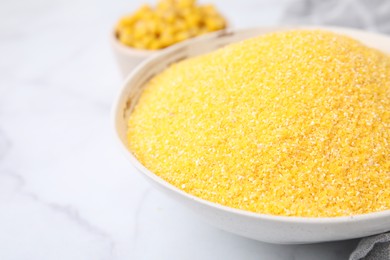 Raw cornmeal in bowl on white marble table, closeup. Space for text