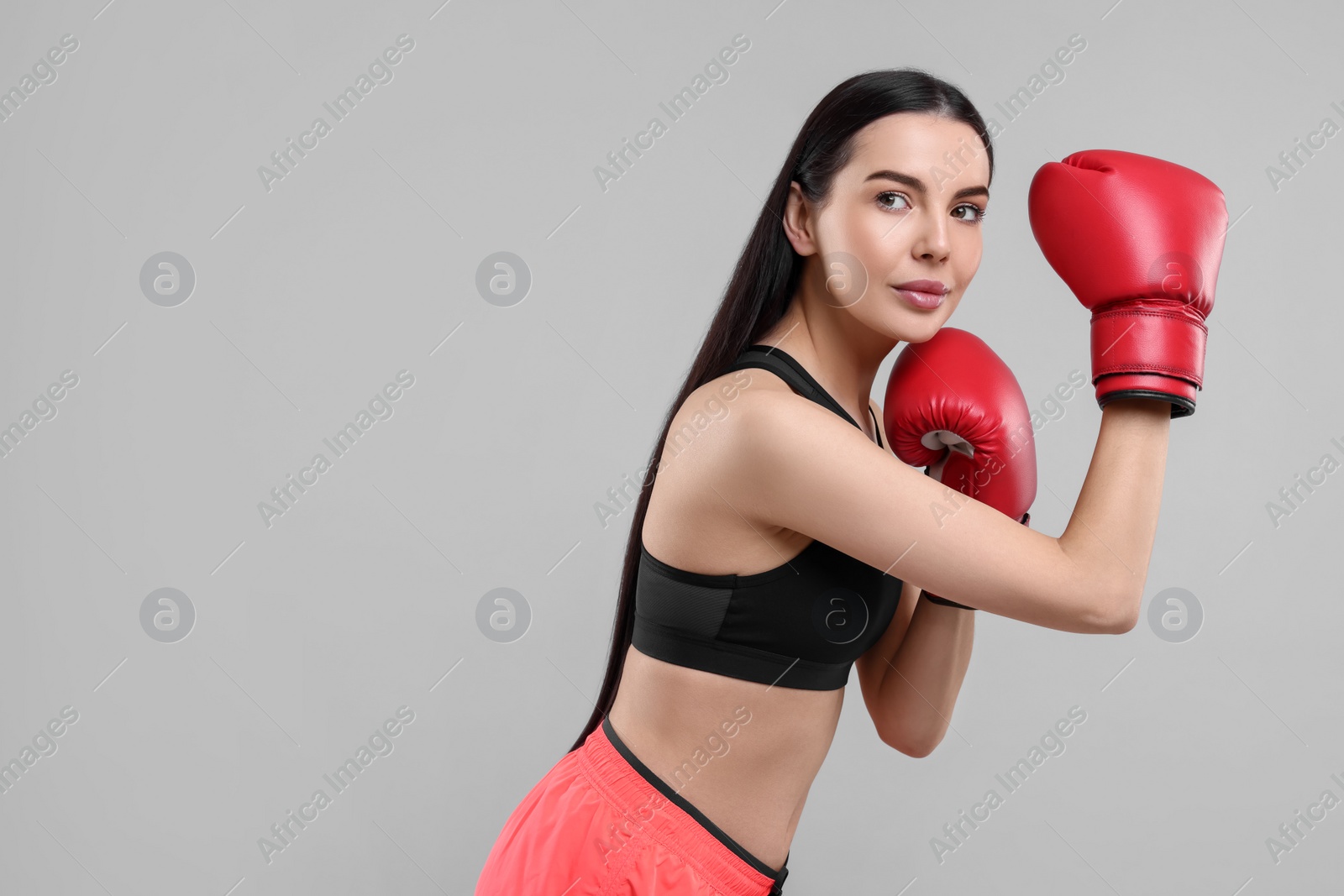 Photo of Portrait of beautiful woman in boxing gloves on grey background. Space for text