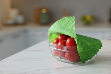 Tomatoes in bowl covered with beeswax food wrap on white table indoors, closeup. Space for text