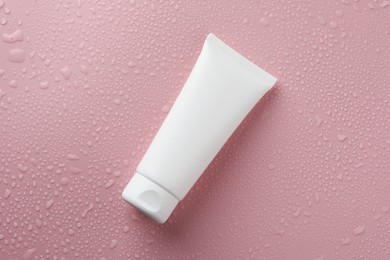 Moisturizing cream in tube on pink background with water drops, top view