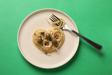 Photo of Heart made of tasty spaghetti, fork, olives and cheese on green background, top view