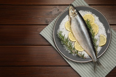 Photo of Delicious salted herring, rosemary, salt and lemon on wooden table, top view. Space for text