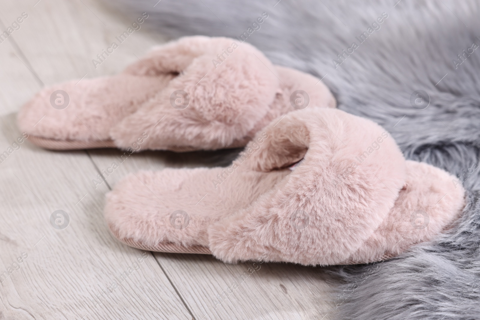 Photo of Pink soft slippers on light wooden floor at home, closeup