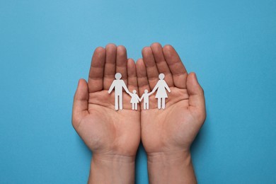 Photo of Man holding paper family figures on light blue background, top view. Insurance concept