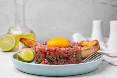 Photo of Tasty beef steak tartare served with yolk, toasted bread and lime on white table