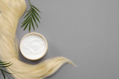 Lock of healthy blond hair, green twigs and cosmetic product on grey background, flat lay. Space for text