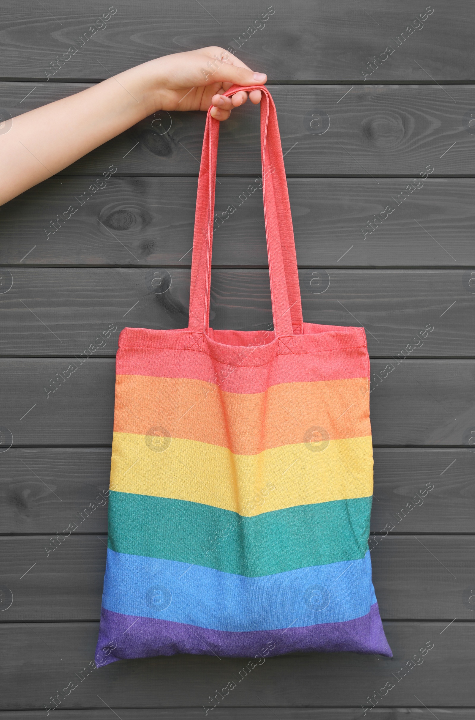 Photo of Woman holding rainbow bag against grey wooden background, closeup. LGBT pride